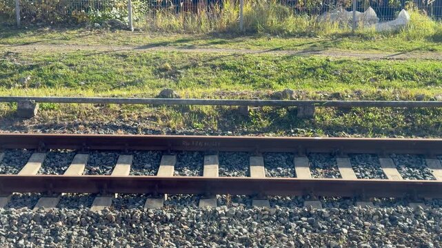 Steel railway tracks with concrete sleepers on gravel ballast along green grass embankment. Industrial railroad transport infrastructure, passenger train line logistics and heavy engineering path.