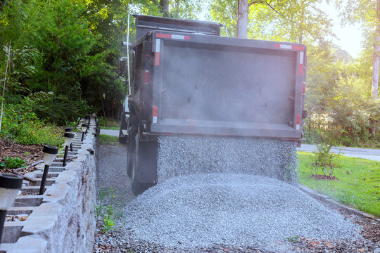 Heavy dump truck dumps gravel on yard while dust rises is neighborhood