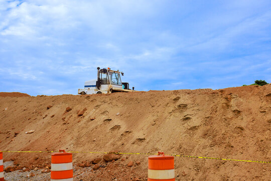 Machine is operating on dirt mound at construction site orange barriers mark area around work site.