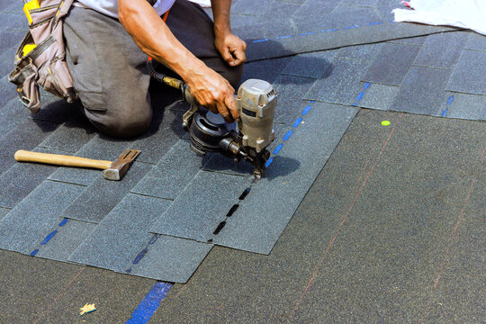 Builder uses air pneumatic nail gun to secure shingles on roof