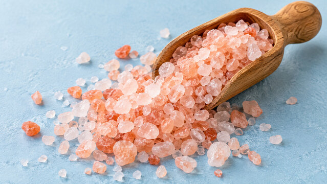 Coarse pink salt spilling from a small wooden scoop