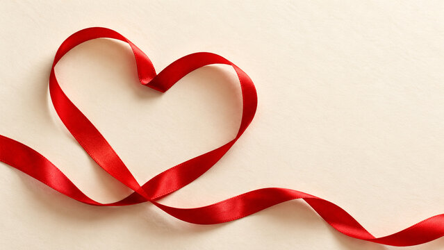 Red satin ribbon forming a heart on a cream background