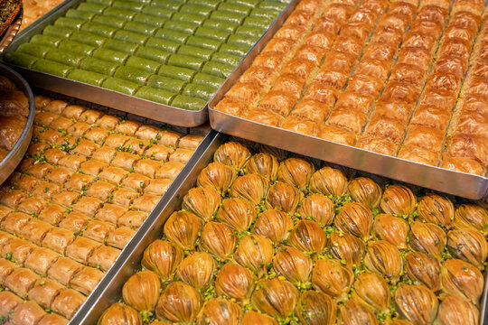 Assortment of traditional Turkish baklava varieties in metal trays including pistachio wrap and midye baklava
