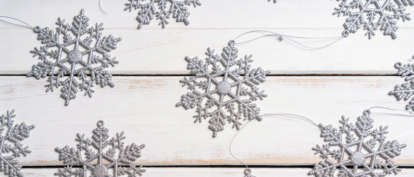 Silver snowflake ornaments are arranged on a white wooden plank background in a top view composition.