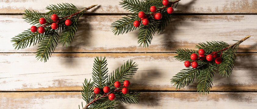 Fir branches with red berries are arranged on a rustic whitewashed wooden surface in a top-down view.
