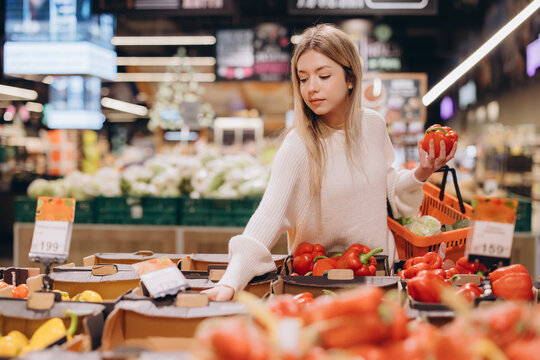 Woman choosing bell peppers in supermarket produce section