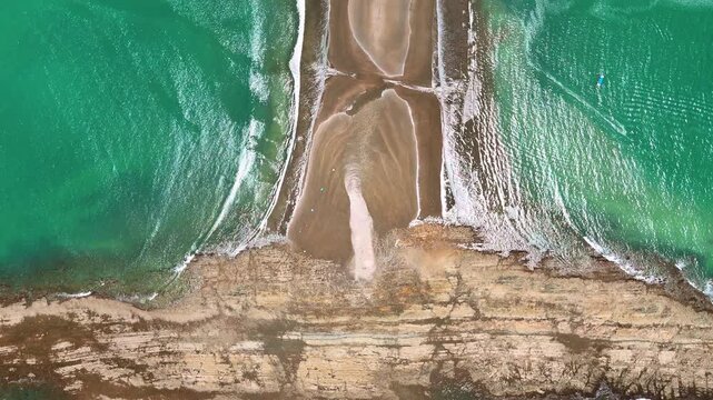 The Uvita tombolo joins an exposed rock platform. Parallel bands of white surf border a narrow sandy strip above textured coastal rock.