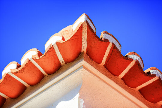 Terracotta roof tiles on corner of Mediterranean house eaves against clear sky, low angle view of clay tile edge with plastered wall for architecture, real estate, construction