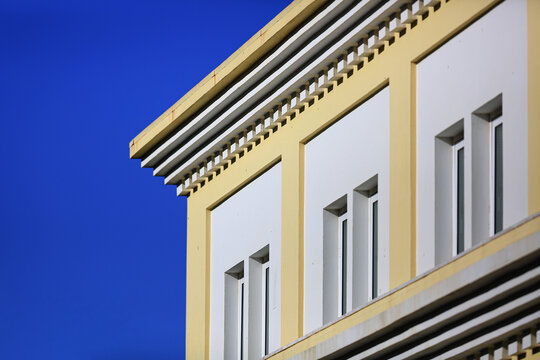 Pastel building facade with cornice dentils and recessed windows against clear sky, sunlit architecture detail with selective focus for real estate, construction and modern urban design concepts