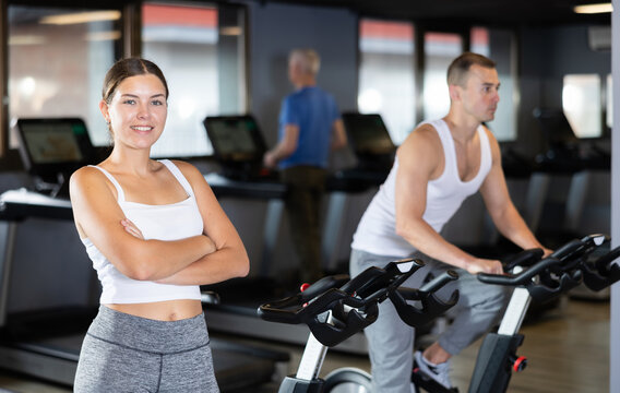 Young athletic woman posing by exercise bike in gym