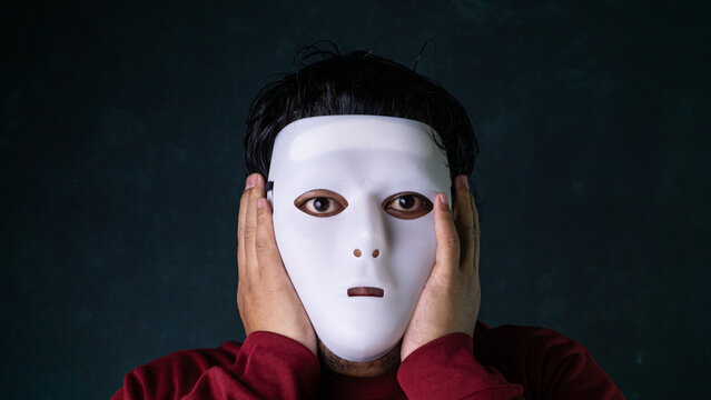 An anonymous man wearing a white disguise holds both hands over his covered ears under dramatic lighting against a dark green textured background, illustrating sensory overload. This