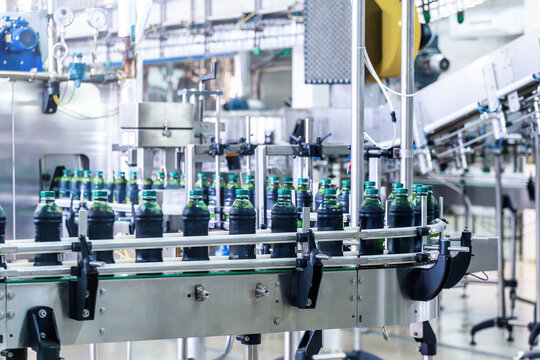 Automated beverage bottling and packaging line with capped plastic bottles of dark liquid moving on conveyor, mass production, food manufacturing and industrial automation in factory