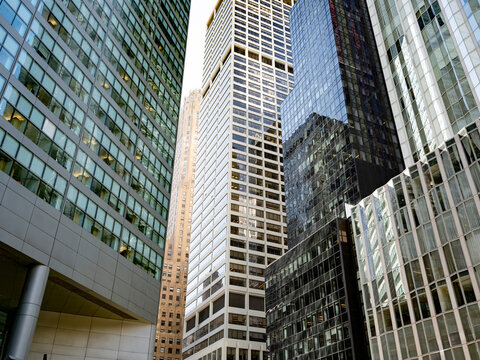 Low angle views of glass and dark-clad office towers with reflections and varied facade patterns in Midtown Manhattan, New York City.