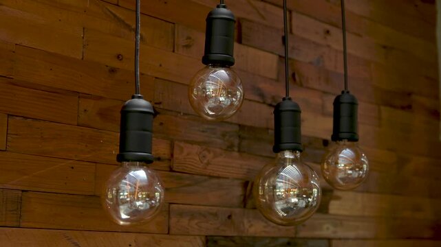 Four Hanging Edison Style Glass Pendant Bulbs Against a Rustic Wooden Wall, Industrial Interior Lighting, 4K 60fps Video