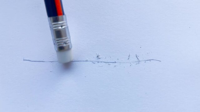 Close Up Of A Pencil Eraser Rubbing A Graphite Line On Textured White Paper, Leaving Small Eraser Crumbs.  Concept Of Correcting Mistakes, Revision, And Starting Over.