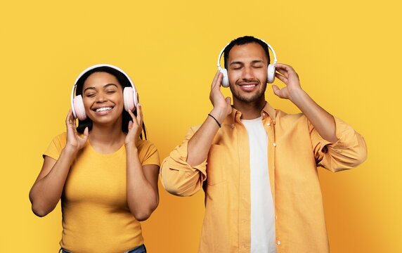 Smiling Young Black Man And Woman Enjoying Music Together With Headphones On In Casual Atmosphere, Studio Setting, Creating Vibrant And Joyful Environment.