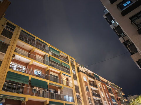 Social housing facades rise above a street at night, in valencia, spain, showing apartment buildings that form part of the city's residential fabric.