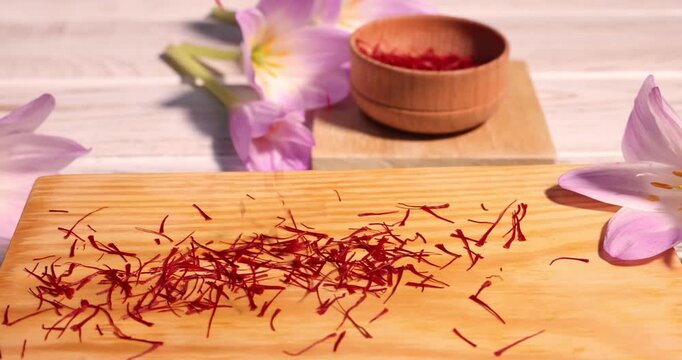 Sprinkling saffron onto board near crocus flowers on light wooden table, closeup