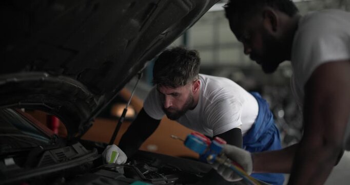 Two mechanics inspecting car air conditioning system with manifold gauge and flashlight
