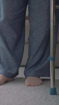 Senior woman recovering from illness trying to walk again using a four-legged crutch.