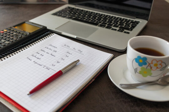 Angled view of workspace with laptop, budget notebook, calculator, and coffee