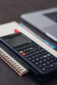 Close-up shot of scientific calculator on spiral notebook with laptop on dark surface