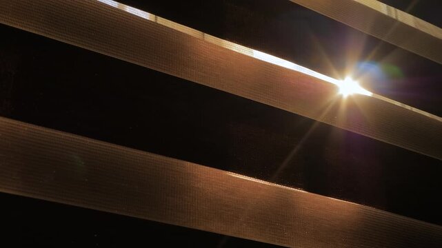 Sun light is shining through the window blinds - view from dark room: sun lens flare, close up, selective focus. Morning, indoors and abstract concept