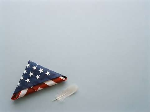 Folded american flag and feather rest on a pale blue background