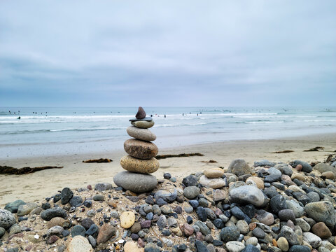 Cairn or beach pebble pyramid standing as a calm symbol of spiritual harmony and wellness built on top of a small sandy mound in Tourmaline surfing park, San Diego, California