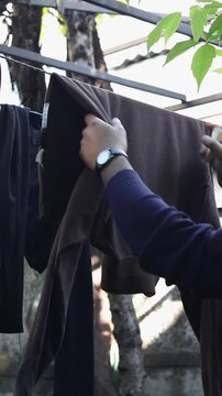Slow motion Person taking down brown garment from clothesline outdoors
