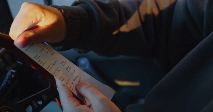 Side view of a person holding and examining a fuel receipt, checking the total cost and itemized charges. Slow-motion 4K video representing fuel prices and everyday expenses.