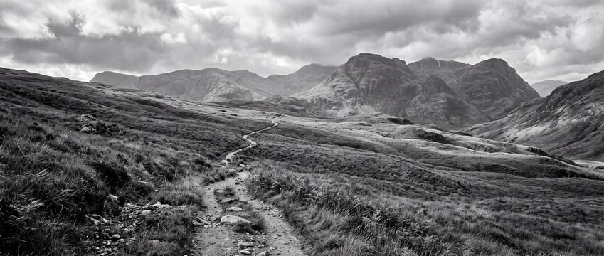 Mountain landscape panoramic view featuring winding hiking trail through dramatic rocky highlands under cloudy sky