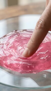 Finger Pressing Into Pink Cosmetic Gel Texture on a Glass Surface