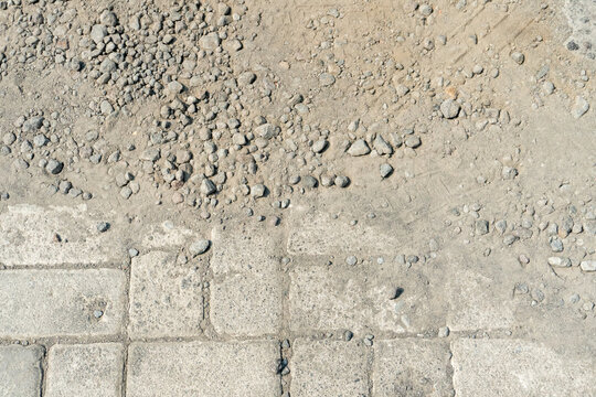 Interlocking gray concrete blocks often referred to as paving blocks are being installed, with their edges bordered by a layer of loose aggregate, sand, and gravel. 