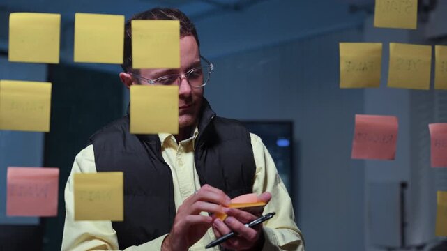 professional software developer planning project strategy using sticky notes on glass wall in modern office workspace teamwork brainstorming startup innovation