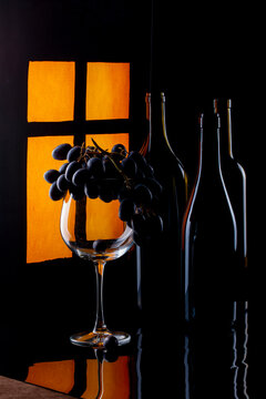 Still life with a bunch of grapes and a bottles near a lit window.