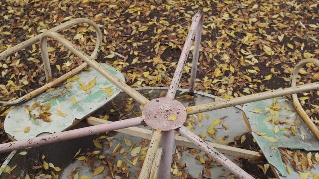 Close up of a rusty vintage metal carousel structure rotating counterclockwise on a ground with autumn leaves in slow motion