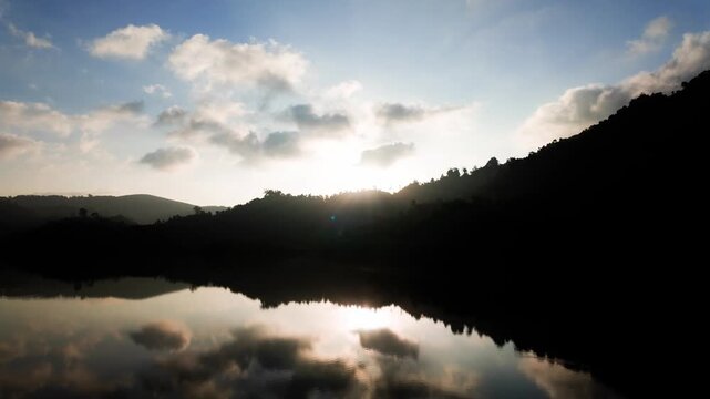 This shows the clear water at Da Lay Irrigation Reservoir in Lam Dong, Vietnam during sunset. The sun sets behind hills, creating a beautiful reflection on the water surface.