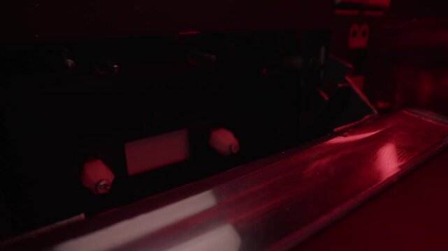 Hand loads a cassette tape into a dual deck player under red light. Gritty retro audio recording scene, ideal for police interrogation, wiretap evidence, crime mystery, and forensic thrillers.