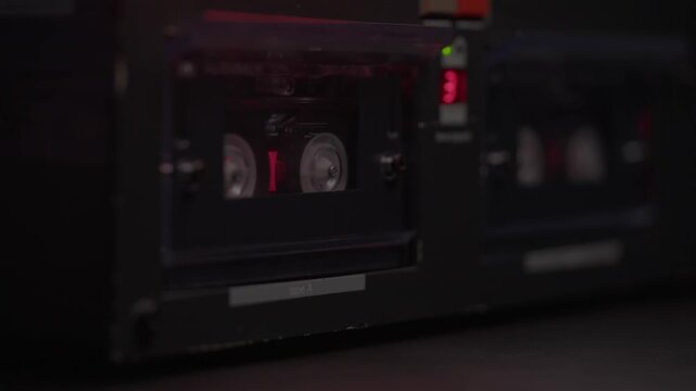 Hand loads a cassette tape into a dual deck player under red light. Gritty retro audio recording scene, ideal for police interrogation, wiretap evidence, crime mystery, and forensic thrillers.