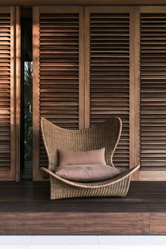 Woven lounge chair with blush cushions before wooden shutters in tropical modernist beach club