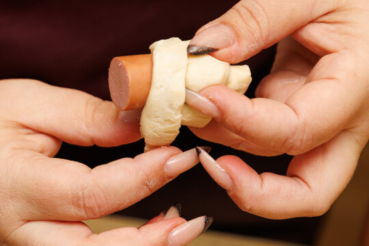 Close-up of hands wrapping dough around a sausage