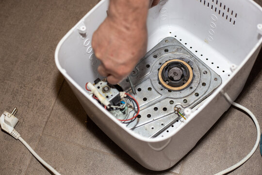A technician installs and screws down the metallic base plate mechanism inside a breadmaker chassis. Home appliance internal repair process. Home Improvement theme.