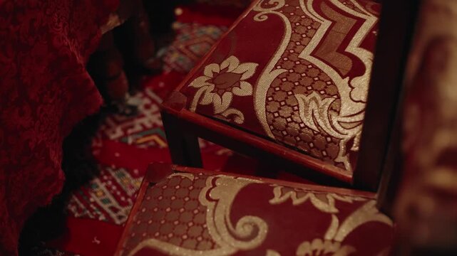 Traditional salon furniture with damask upholstery and wooden legs on a patterned carpet, close detail of interior textiles in Morocco.