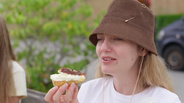 Mother eating a cream filled pastry while sitting beside daughter on a bench slow motion the daughter watches her mother eat