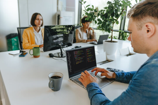 Programmer writes code on laptop at desk in modern office