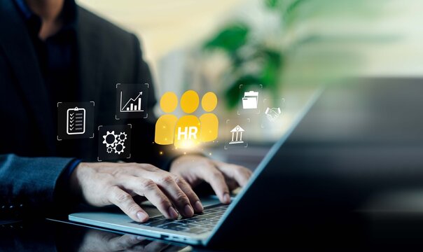 Business person typing on a laptop with a glowing yellow HR human resources icon and management interfaces. Concept of talent acquisition, workforce administration, and personnel management.