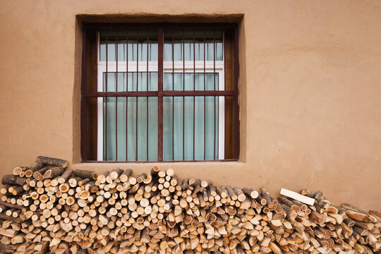 Stack of firewood logs under barred window on brown wall china