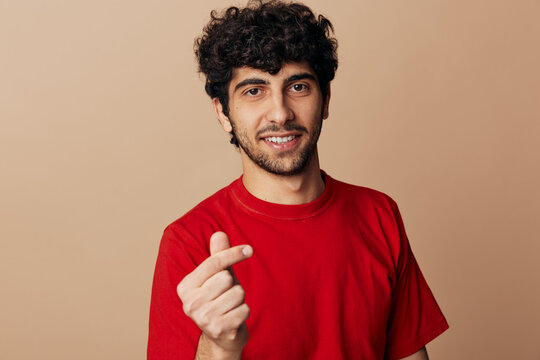 Client testimonial review, smiling young man showing finger heart gesture. Studio portrait on a beige background, friendly mood, positive emotion, warm look, confidence