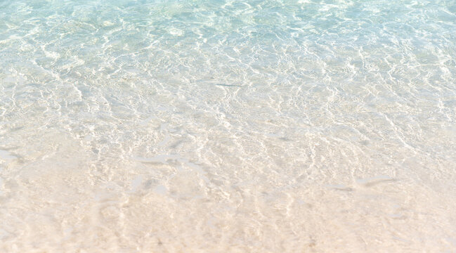 Crystal clear shallow ocean water washing gently over white sand beach shore during bright sunny day in tropical island paradise